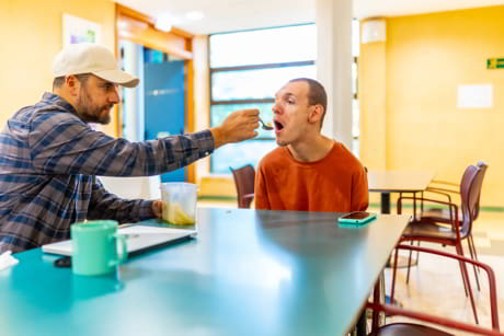 técnico sociosanitario ayudando a comer a un hombre discapacitado